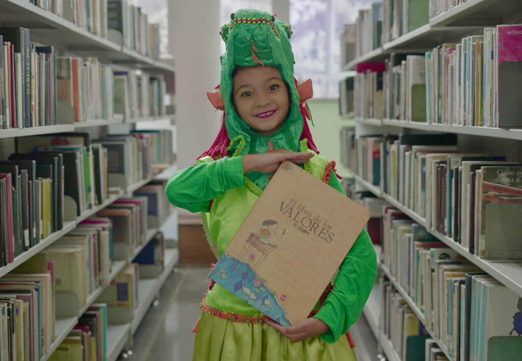 Imagen de niña disfrazada cargando un libreo en una biblioteca