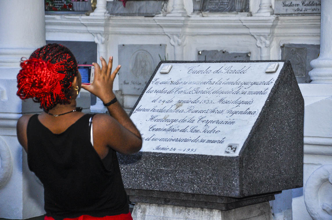 Imagen de una mujer tomando una foto en la tumba de Carlos Gardel